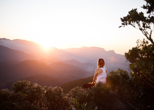 Shot of a woman sitting on mountain top and looking at the sunrise