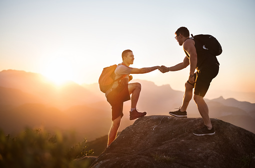 Shot of a two young men on mountain peak climbing and helping each other
