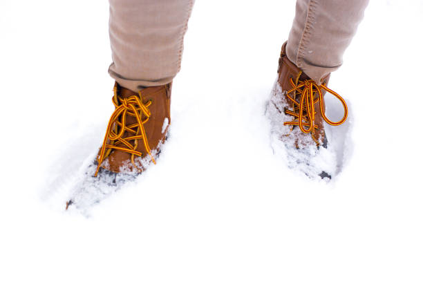 Low angle view of walking away female legs with white snow boots on, in deep snow. Winter background.