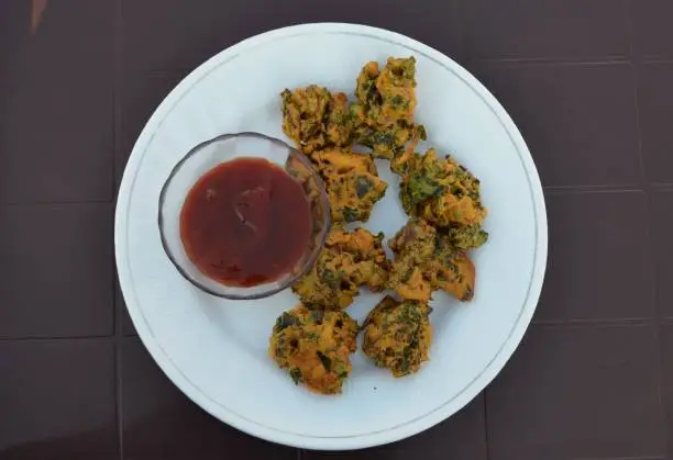 Indian traditional salted fried snack pakora or pakoda. They are made with gram flour by mixing with different vegetables such s spinach, onion, potatoes, cauliflower, fenugreek leaves, green chillies, garlic,salt and spices. Eaten with sauce or chutney.