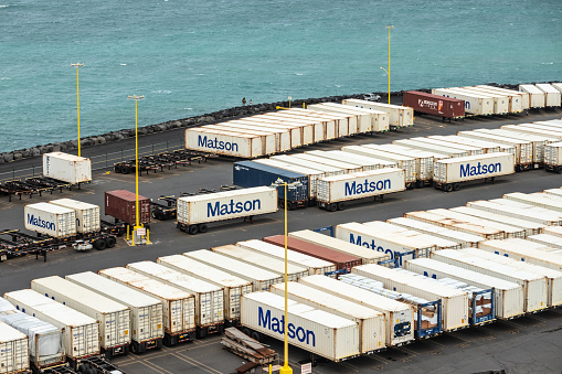 Kahului, Maui,, Hawaii, USA. - January 13, 2020: Closeup of Matson shipping container yard filled with white boxes on trailers on quay bordering azure ocean.
