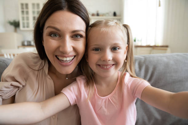 Happy young mom and little daughter making selfie Smiling young mother and small preschooler daughter look at camera making selfie at home together, happy funny mom and little girl child have fun laugh take photo posing for self-portrait picture nanny photos stock pictures, royalty-free photos & images