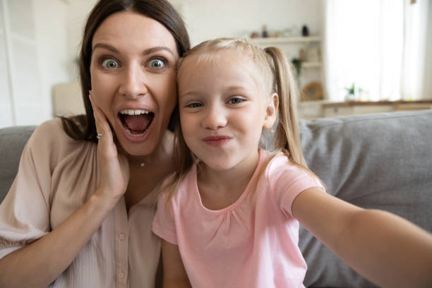 istock Funny young mom and little daughter posing for selfie 1204066322