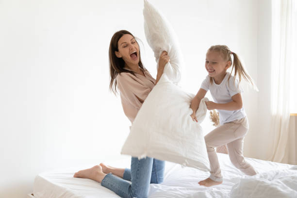 大喜びの小さな女の子と若いお母さんは枕の戦いに従事 - pillow child play family ストックフォトと画像