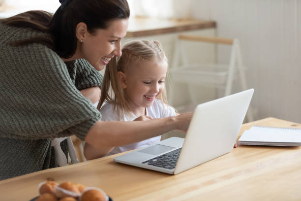 Smiling mother and small daughter using laptop together