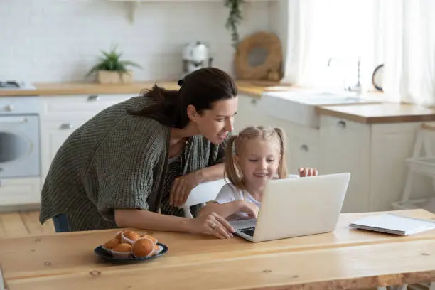 Photo of Young mom and little daughter using laptop together