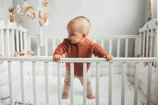 Beautiful little girl in a crib in a cozy light room in a sweater of fashionable shades. learns to stand at the support. Beautiful little girl in a crib in a cozy light room in a sweater of fashionable shades. learns to stand at the support. cheerful little girl standing in the crib at home crib stock pictures, royalty-free photos & images