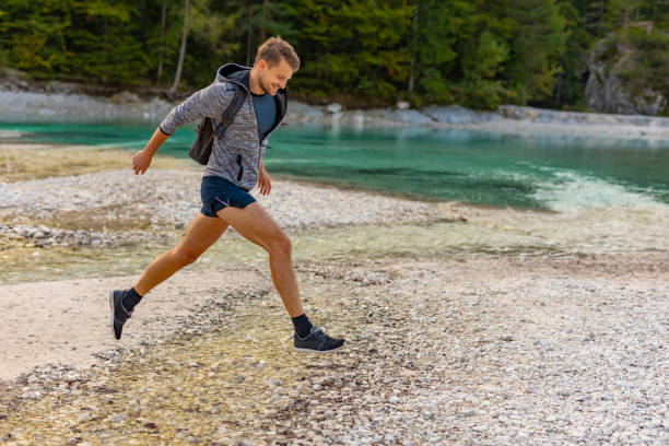 istock Man Jumping Over a River Stream in the Alps 1204076375