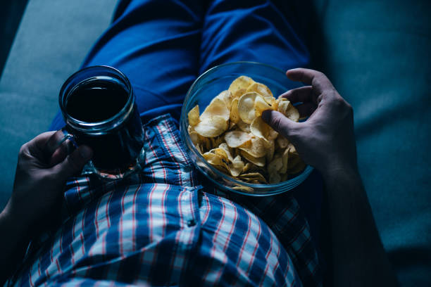 overweight man watching tv with junk food and beer - remote fat overweight dieting imagens e fotografias de stock