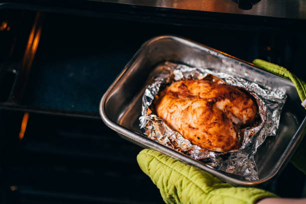 istock Woman taking baked chicken breasts from oven 1204077225