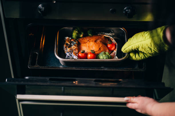 istock Woman taking baked chicken breasts from oven 1204077339