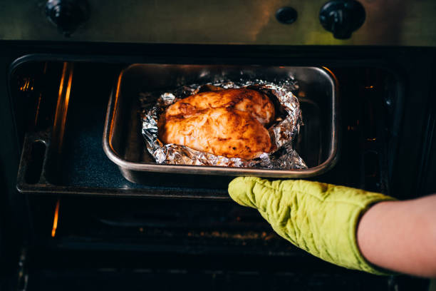 istock Woman taking baked chicken breasts from oven 1204077388