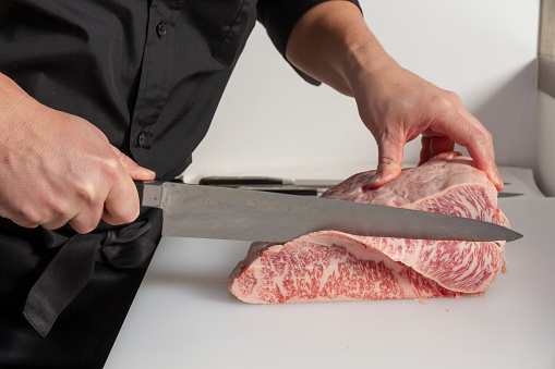 Mature butcher grabbing a block of meat to slice it at the butcher's shop - People at work concepts