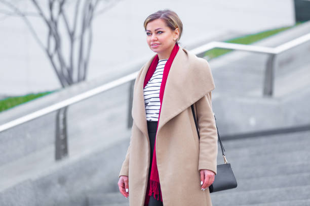 at the mall lifestyle fashion portrait of stunning brunette girl. walking on at the mall. going shopping. wearing stylish white fitted coat, red neckscarf. business woman. black bag - neckscarf imagens e fotografias de stock