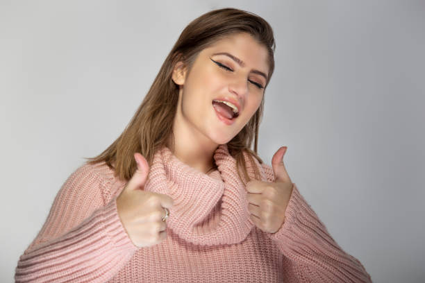 portret młodej kobiety ubranej w różowy sweter z kciukami w górę - endorsement appreciate validate thumbs up zdjęcia i obrazy z banku zdjęć