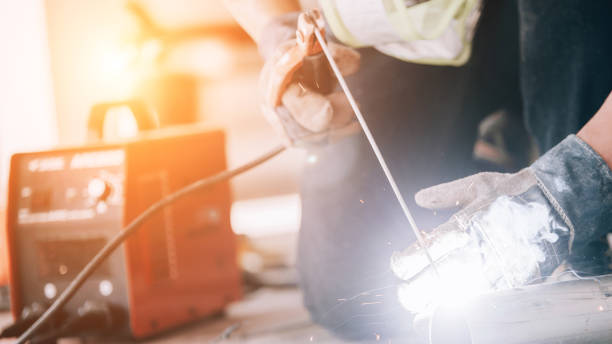 istock Welder in protective uniform and mask welding metal pipe on the industrial table while sparks flying. 1204088171