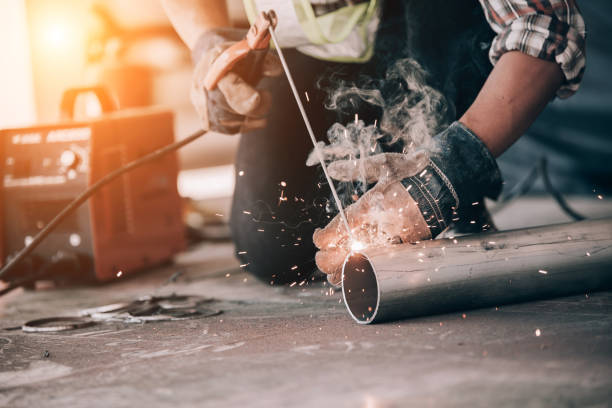 istock Welder in protective uniform and mask welding metal pipe on the industrial table while sparks flying. 1204088235