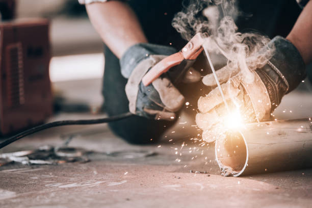 istock Welder in protective uniform and mask welding metal pipe on the industrial table while sparks flying. 1204088237