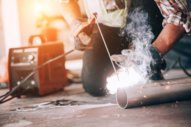 istock Welder in protective uniform and mask welding metal pipe on the industrial table while sparks flying. 1204088253