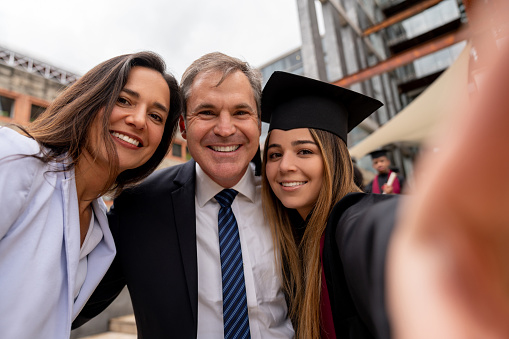 Portrait of a happy graduating student taking a selfie with her parents on graduation day