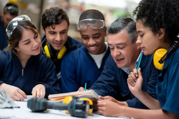 Teacher talking to a group of industrial design students in class and writing notes on his notebook