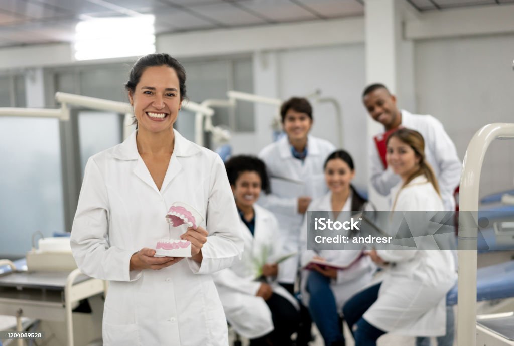 Happy teacher at dental school holding a prothesis and smiling Happy teacher at dental school with a group of students holding a prothesis and looking at the camera smiling Dental Health Stock Photo