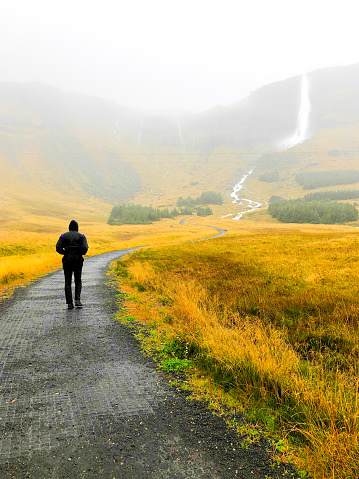 Snaefellsnes, Iceland: A hiker walking toward Bjarnarfoss Waterfall in the rain.