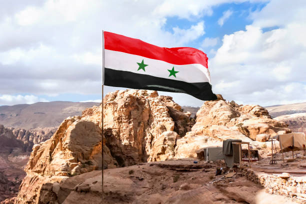 flaga syrii na maszcie trzepocze na wietrze pod niebem. syryjska flaga jest ustawiona na wysokości w górach na tle natury bliskiego wschodu. - qunaitira zdjęcia i obrazy z banku zdjęć