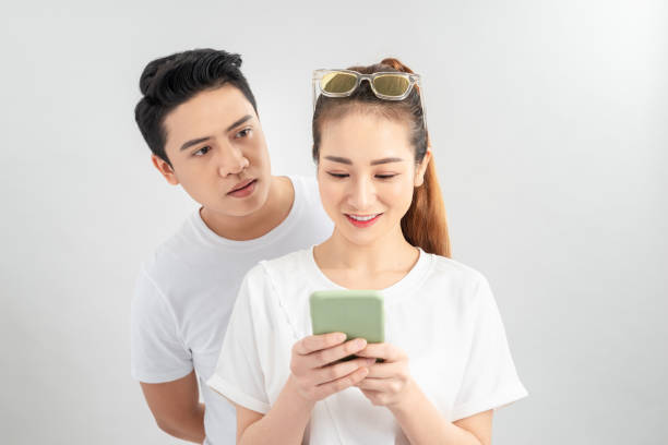 istock Attractive suspicious young couple standing isolated over white background, using mobile phone 1204097455