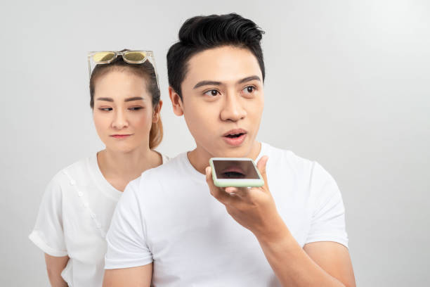 istock Attractive curious young couple standing together isolated over white background, using mobile phone 1204097456