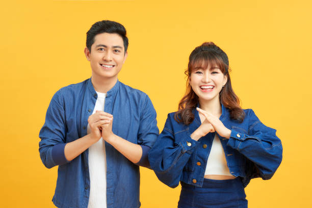 istock Young couple posing in a yellow background clasping hands at camera in congratulations gesture. 1204101721