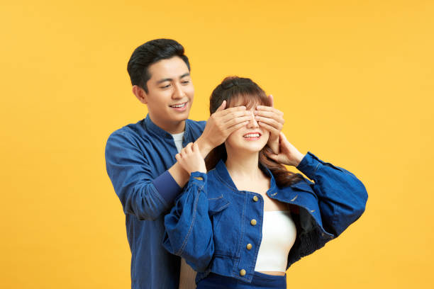istock Guess who. Playful young guy standing behind girlfriend and closing her eyes, yellow studio background with copy space 1204102554