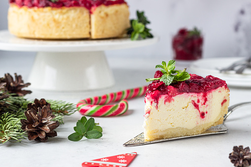 Classical New York cheesecake with cranberry sauce, mint and rosemary, light grey stone background. Festive Christmas decoration.