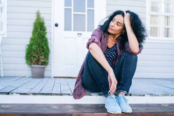 Sad mid adult woman sitting on stairs in front of her house Sad mid adult woman sitting on stairs in front of her house disappointment stock pictures, royalty-free photos & images