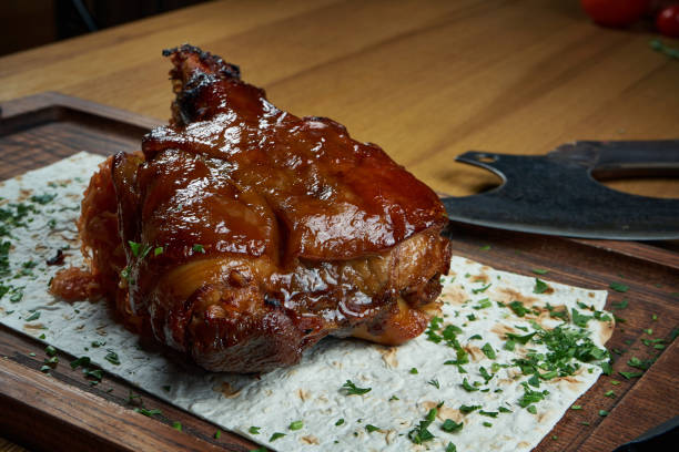 a classic dish of german and czech cuisine is pork shank in beer and honey sauce on a wooden board. beer snack. tasty food close up. roasted pork knuckle eisbein - shank sauerkraut german cuisine pork imagens e fotografias de stock