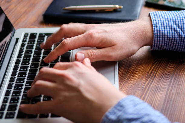 istock A man in a shirt works behind a laptop typing text. 1204123288