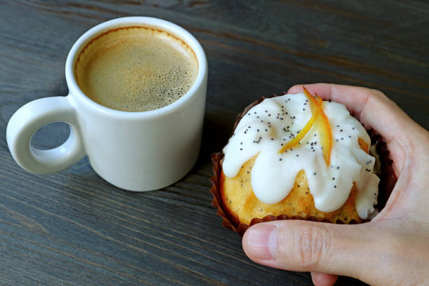 Hand holding an orange yogurt cake with a cup of hot coffee in background