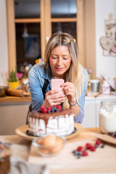 istock Woman baking at home: Photographing her chocolate sponge cake with berries 1204128406
