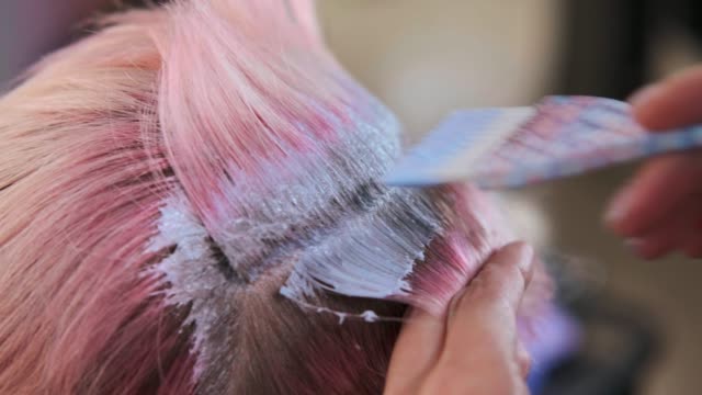 Hairdresser colorist puts paint on hair of woman client.