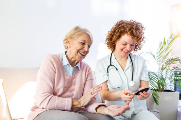 happy senior woman having her blood sugar measured in a nursing home by her caregiver. happy nurse measuring blood sugar of a senior woman in living room - diabetes and glicemia concept - diabetes home interior blood sugar test healthcare and medicine imagens e fotografias de stock