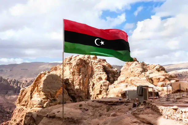 Flag of Islamic republic of Libya waving in mountain background and cloudy skies