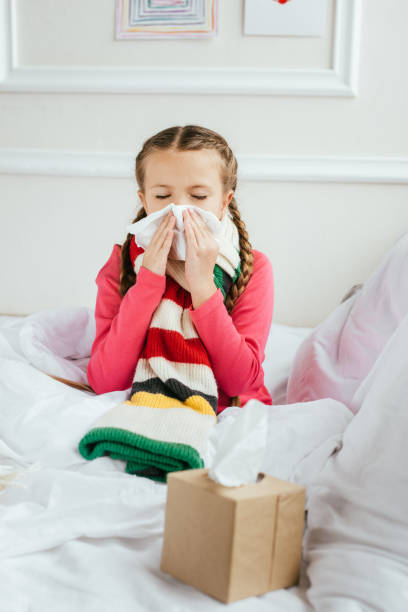 istock sick kid with runny nose holding napkins while sitting on bed 1204142653