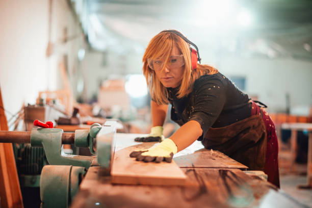 istock Female carpenter pushing a plank to cut it using a saw guide 1204143119