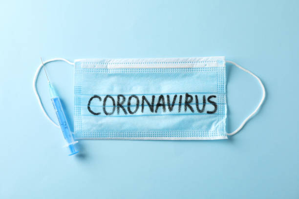 istock Protective mask with inscription Coronavirus and syringe on blue background, top view, space for text. 1204143412