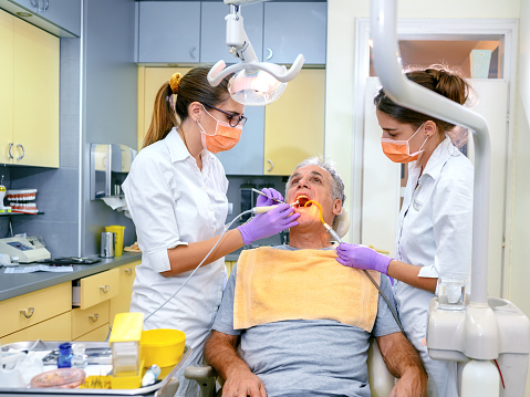 Female dentist treating patient mature man teeth.