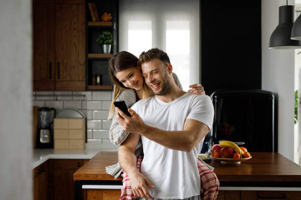 istock Young affectionate couple looking at mobile phone in the kitchen 1204145752