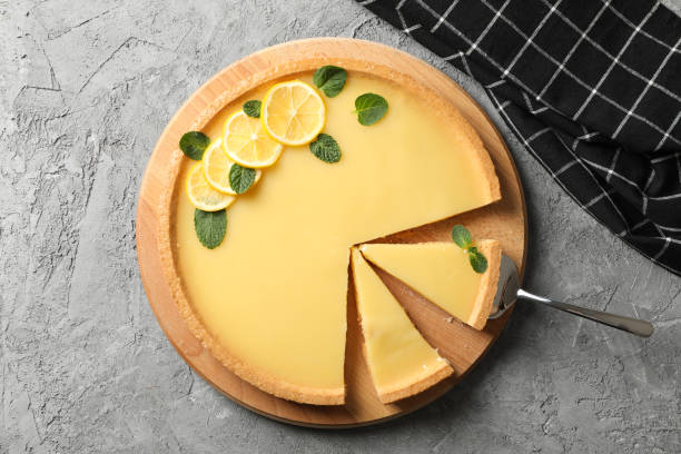 istock Wood board with lemon tart on grey background with towel, top view 1204147075
