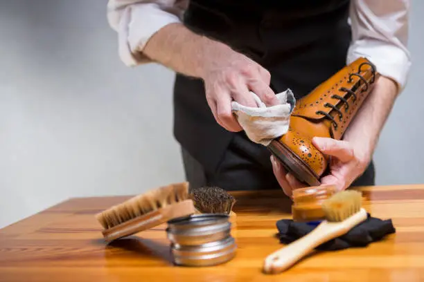 Photo of Footwear Concepts and Ideas. Closeup of Hands of Man Cleaning Premium Derby Boots With Variety of Brushes and Accessories.Horizontal Image