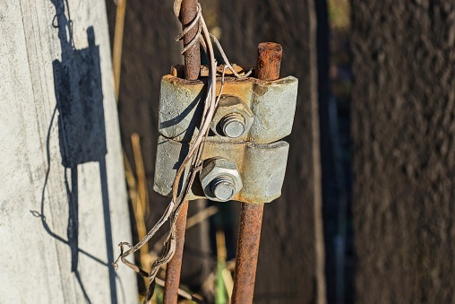 lightning conductor with grounding from gray iron plates on nuts and bolts on steel rusty rods with wire on the street