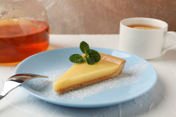istock Plate with lemon tart slice, teapot and cup of tea on white table, close up 1204149059